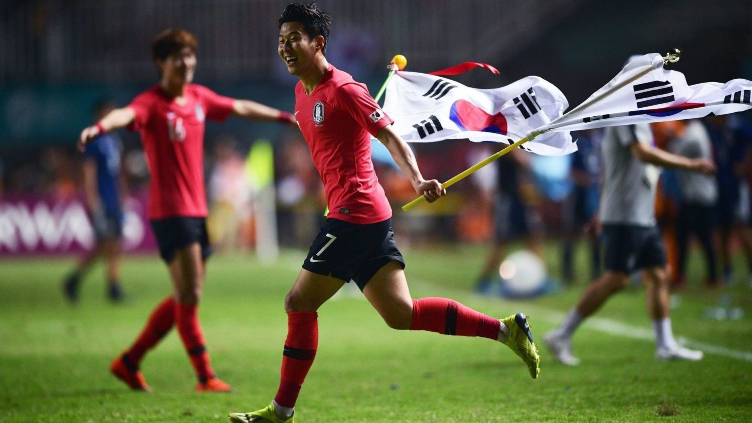 Son Heung-Min festeggia la vittoria nei giochi asiatici 2018 sventolando due bandiere della Corea del Sud. Foto: AFP.