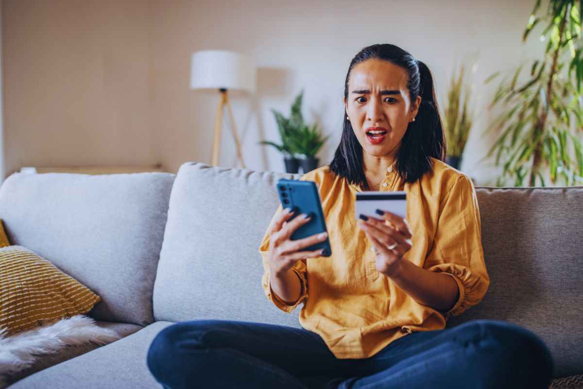 Donna con espressione sconvolta tiene il telefono in una mano e la carta di credito nell'altra