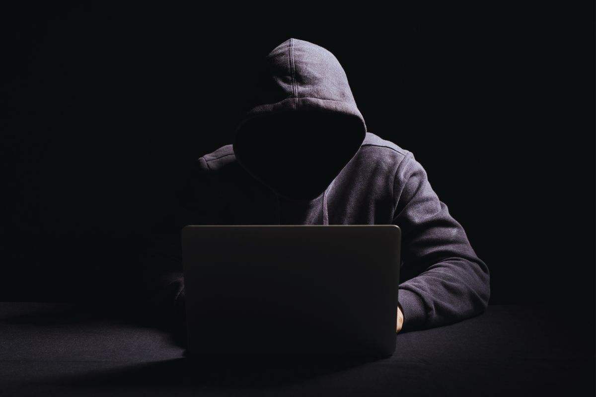 Uomo con volto coperto da cappuccio che utilizza un PC