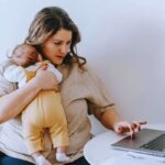 Donna che utilizza computer con neonato in braccio