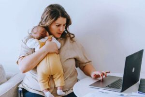 Donna che utilizza computer con neonato in braccio
