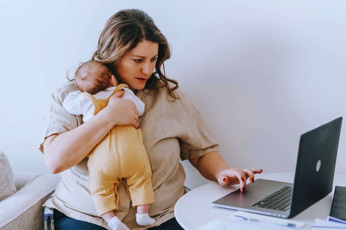 Donna che utilizza computer con neonato in braccio