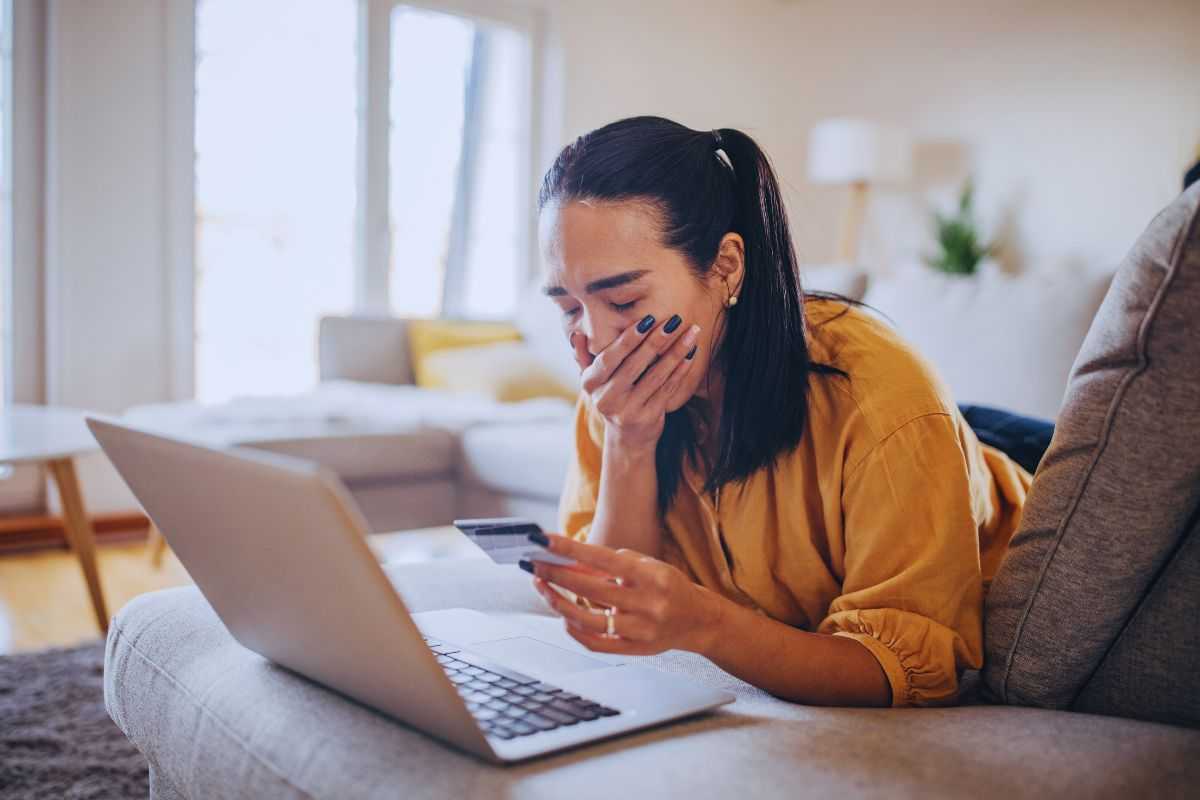 Donna disperata si porta una mano al viso e tiene con l'altra una carta di credito