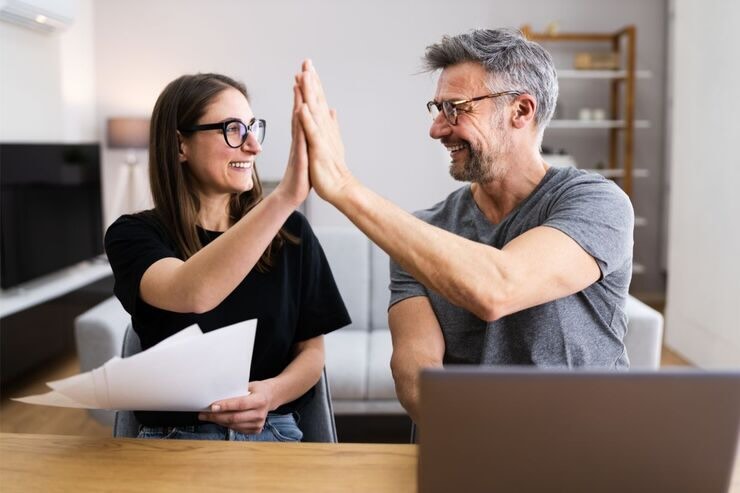 Uomo e donna si battono 5, lei ha fogli in mano e lui davanti ha il PC 