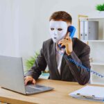 persona con una maschera al computer e al telefono