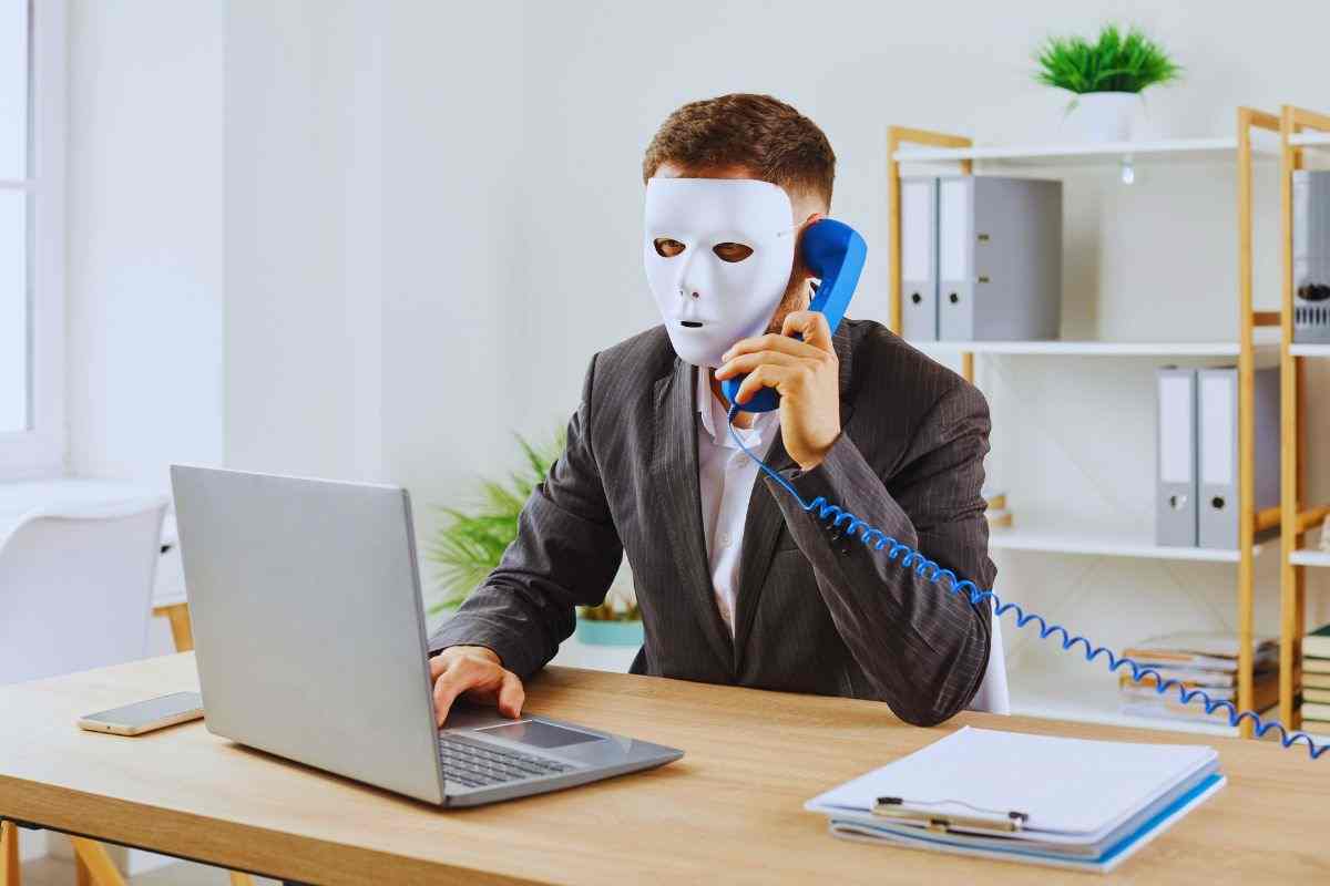 persona con una maschera al computer e al telefono
