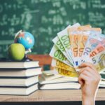 sfondo lavagna e banco con libri e mano che mostra banconote