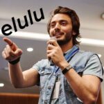 giovane che parla al microfono, scritta delulu